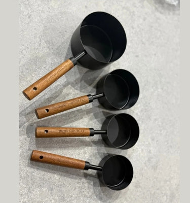 Set of four black measuring cups with wooden handles on a textured surface